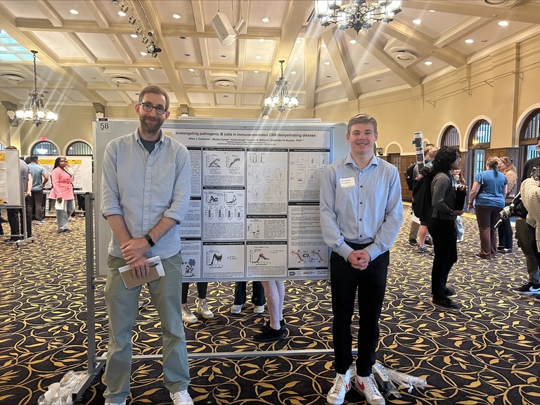 Alex and Miles standing in front of a research poster, smiling